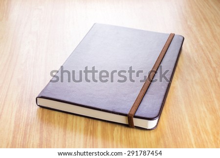 Brown Hard cover notebook with elastic strap on wooden table in perspective view,Template for adding your title.