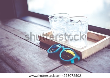 Vintage filter,sunglasses and cold glass of water on wood tray at window of restaurant.