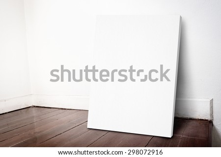 Blank white canvas frame leaning at house wall and dark brown parquet floor, Mock up for adding your design.