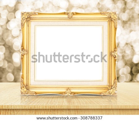 Blank golden vintage photo frame with sparkling gold bokeh wall and wooden table