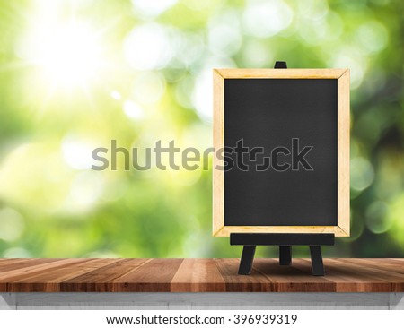 Blank blackboard on wood table top  with sun and blur green tree bokeh background, Template mock up for montage of product.
