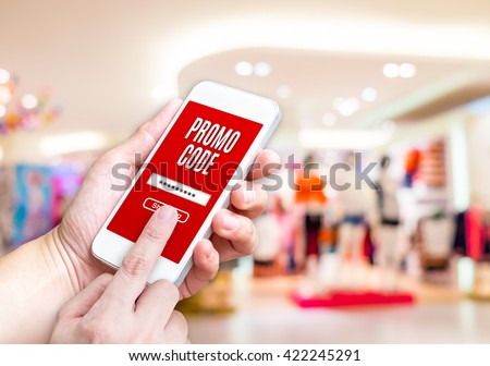 Hand holding mobile phone with promo code word with blurred store background with bokeh light ,internet marketing concept,E-commerce