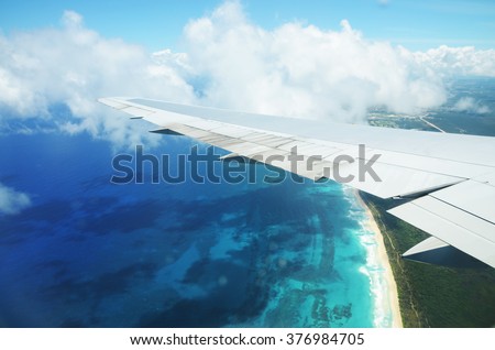 View from airplane window. Wing of an airplane flying above the clouds over tropical island