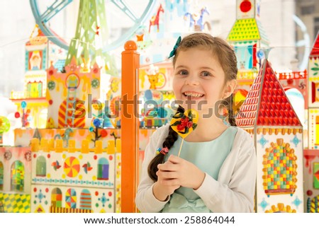 Happy little girl with beautiful eyes smiling at camera and holding lollipop in hands