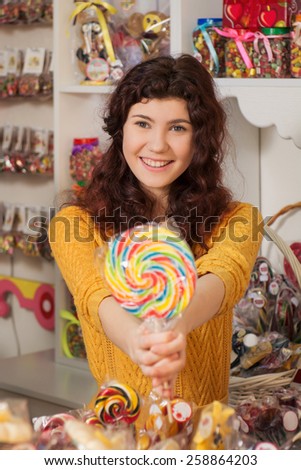 Young woman working in a small busines. Sweets salesman with candy in the hands