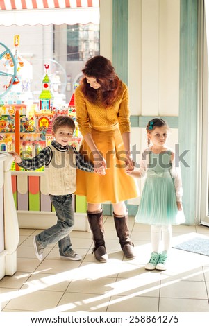 Sad child holding mother by the hand in the children\'s store. Son and daughter holding mother for her  hand