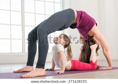 Young mother and daughter doing yoga exercise in fitness studio with big windows on background