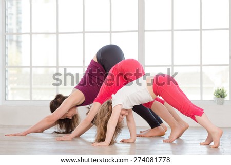 Young mother and daughters doing yoga exercise in fitness studio with big windows on background