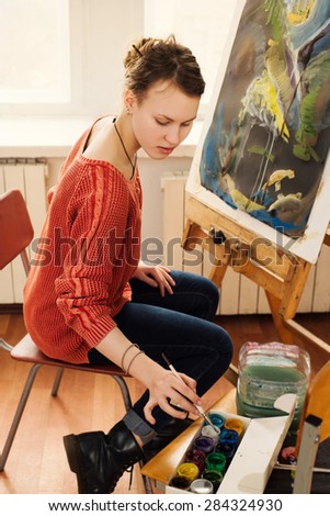 Beautiful woman artist drawing her picture on canvas with oil colors in home art studio