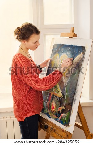 Beautiful woman artist drawing her picture on canvas with oil colors in her workshop