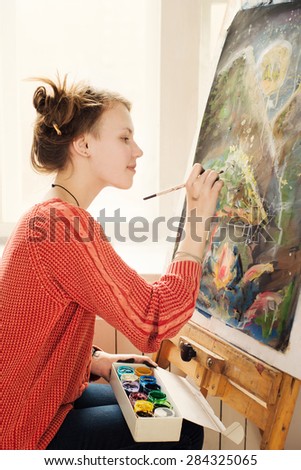 Beautiful woman artist drawing her picture on canvas with oil colors in home studio