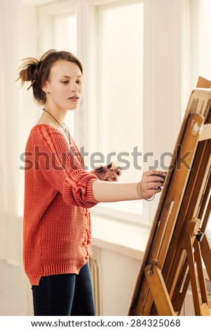Beautiful woman artist drawing her picture on canvas with oil colors in home studio