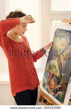Beautiful woman artist drawing her picture on canvas with oil colors in home art studio