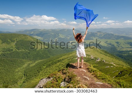 Happy woman enjoying the nature in the mountains with blue tissue in hands on blue sky background