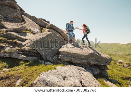 Hiker couple helps each other to climb on the rock in mountains