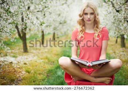 Blond beautiful woman reading a book in the orchard