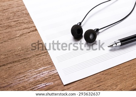 blank sheet music on wooden table with headphones and pen