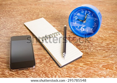 blue alarm clock, mobile phone and notebook on table, business concept