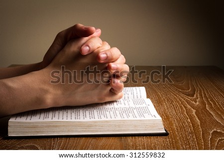 hands folded praying on bible