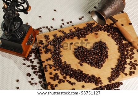 coffee beans in a heart\'s shape on the breadboard with coffee mill and coffee pot