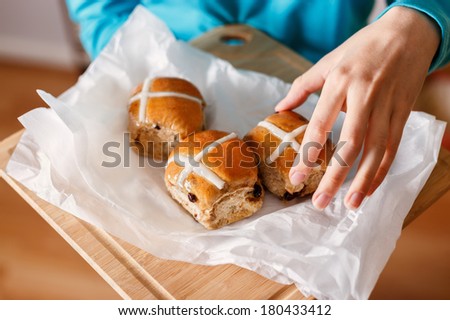 Female hand taking traditional Easter cross-bun and other hand holding cross buns served on white baking paper placed on chopping board
