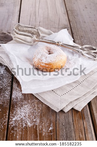 Freshly baked cinnamon sugared doughnuts on baking paper and linen napkin with silver vintage cake tongs on wooden background. Elegant rustic still life