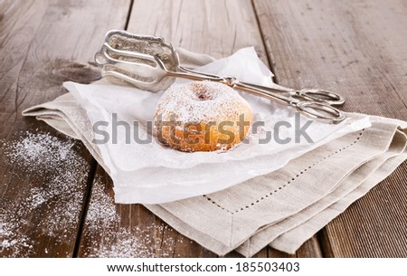 Freshly baked cinnamon sugared doughnuts on baking paper and linen napkin with silver vintage cake tongs on  wooden background. Elegant rustic still life