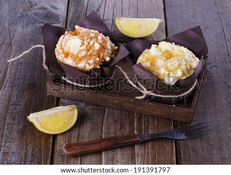 Two lemon flavored muffins and lemon quarters on a rustic dark wooden background