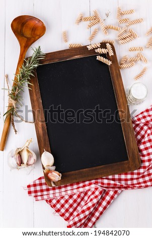 Cooking concept. Menu black board and ingredients for cooking pasta over white wooden background. Top view