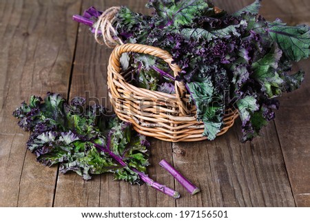 Bunch of organic kale in a woven basket and kale leaf on a rustic wooden background. Selective focus, shallow DoF