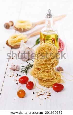 Pasta, tomatoes, garlic, oil and basil over white wooden background
