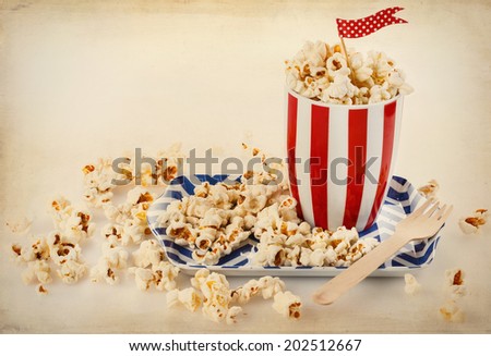 Retro style image of Buttered popcorn in a vintage striped red-white bowl with polka dot flag. Selective focus, vintage filters, textures