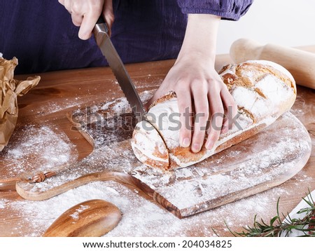 Baker hands cutting rustic sourdough bread on a wooden table