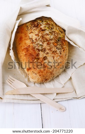 Freshly baked sourdough bread with seeds and grains wrapped in a rustic cloth over white wooden background