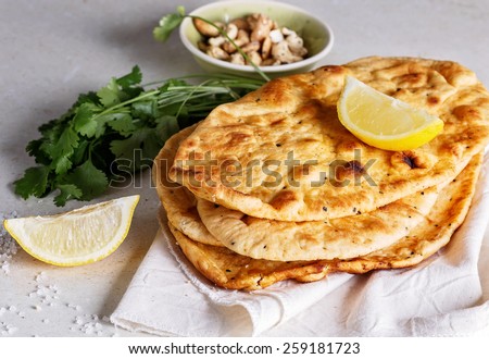Stack of freshly baked flat bread, lemon and coriander on a table