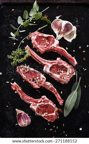 Lamb cutlets with herbs on a black textured metal tray. Top view