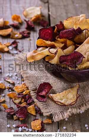 Healthy vegetable beetroot, sweet potato and white sweet potato chips on a black board with spoon of seasoning over rustic background. Top view
