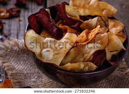 Healthy vegetable beetroot, sweet potato and white sweet potato chips on a black board with spoon of seasoning over rustic background. Top view