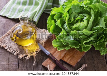 Single organic butter lettuce head on a chopping board and oil over wooden rustic background