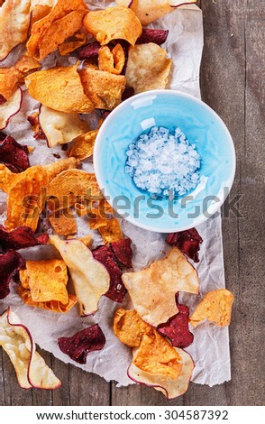 Healthy vegetable beetroot, sweet potato and white sweet potato chips on a black board and sea salt over rustic background. Top view