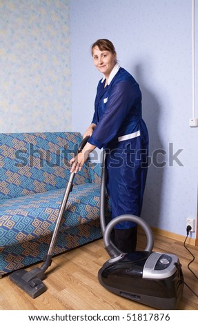 The woman in overalls vacuums a floor
