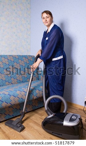 The woman in overalls vacuums a floor