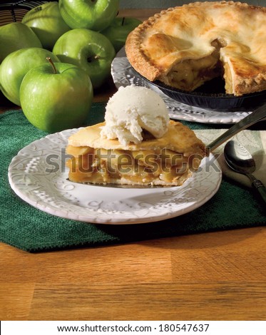 Apple Pie Slice Served with Green Apples and Pie in Background and Vanilla Ice Cream on Top.