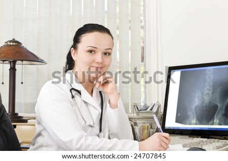 Portrait of female doctor sitting at the table with x-ray scan on the monitor
