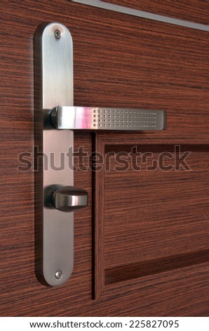 Modern chrome metallic door handle on wooden door