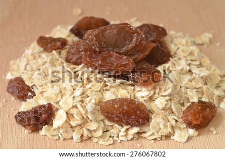 Detail of heap of fine oat flakes and raisins on wooden desk