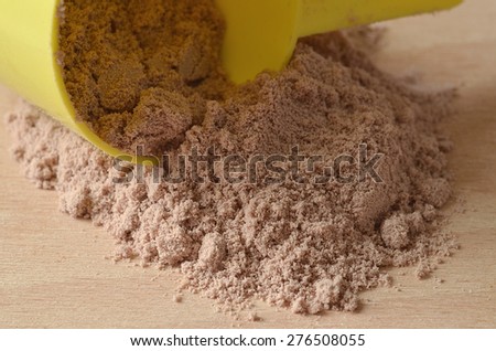 Close-up detail of chocolate protein powder spilled from yellow scoop on wooden desk