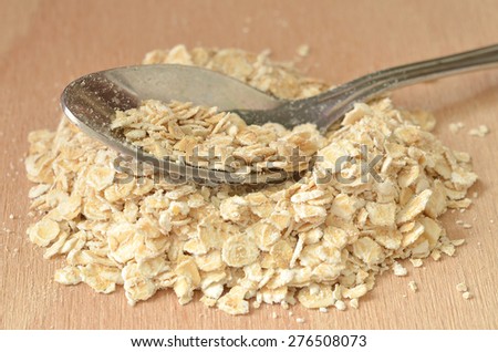 Detail spoon in heap of fine oat flakes on wooden desk