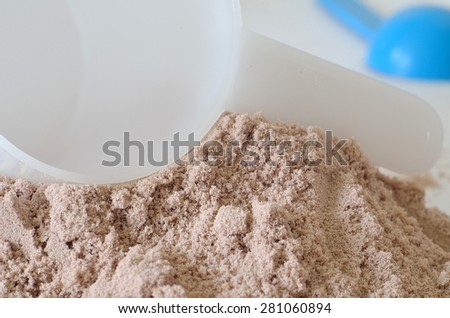 Close-up detail of white scoop in heap of chocolate protein powder and blue scoop in foreground