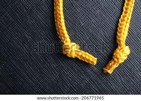 a couple gold color rope cables with simple knot close up photo hanging down in front of the black color artificial leather background.